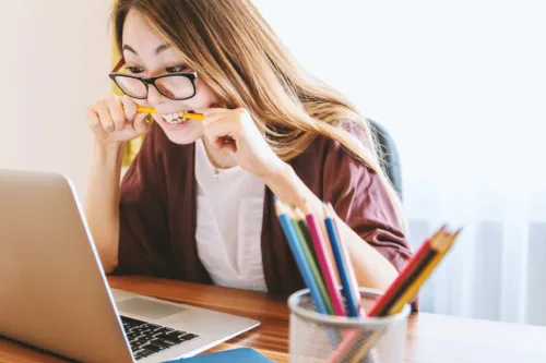 Woman biting a pencil next to a laptop